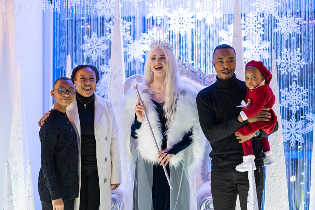 Family with the Winterfest Snow Queen smiling looking at the camera in the Queen's throne room.